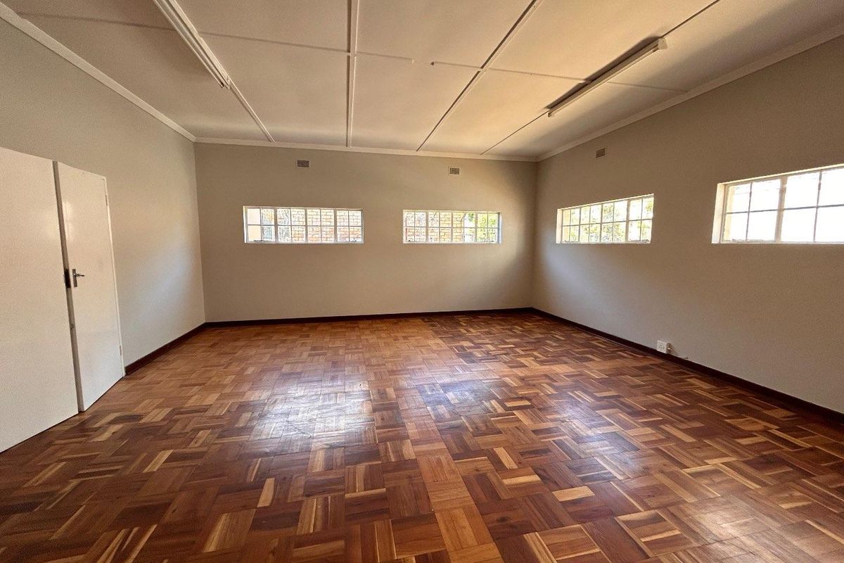 A spacious, empty room featuring traditional parquet wood flooring, multiple high-set windows, and functional overhead lighting, suitable for a variety of uses.