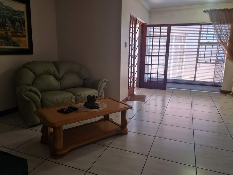 A living room featuring light-colored floor tiles, wooden framed glass sliding doors leading to the exterior, and integrated security gates.