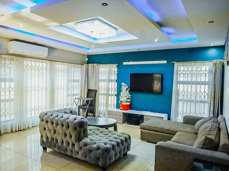 Spacious living room featuring a modern recessed ceiling with integrated LED lighting, tiled floors, and large windows fitted with security gates.