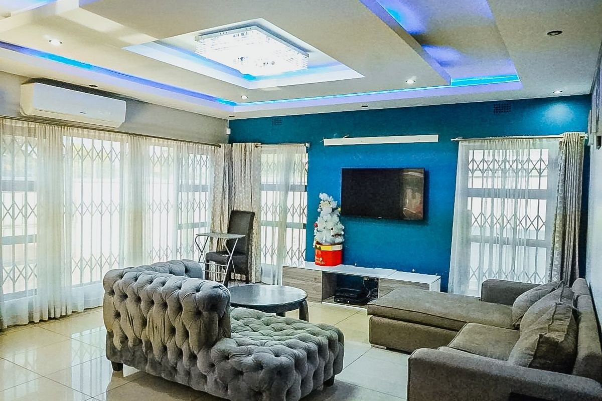 Spacious living room featuring a modern recessed ceiling with integrated LED lighting, tiled floors, and large windows fitted with security gates.