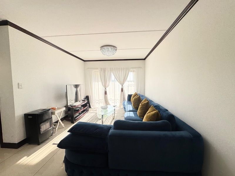 A bright living room featuring tiled flooring, decorative ceiling molding, and a sliding glass door providing natural light.