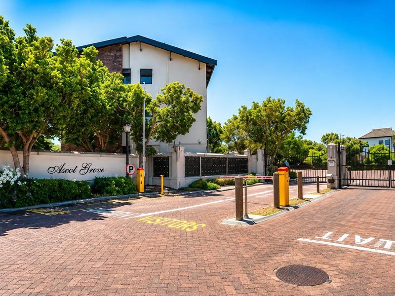 The entrance to Ascot Grove apartment complex featuring a secure boom gate, paved driveway, and well-maintained perimeter wall with integrated post boxes.