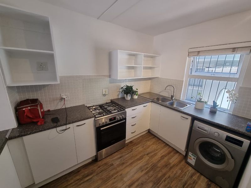 A functional kitchen featuring white cabinetry, a gas stove with oven, double sink, tiled backsplash, and durable laminate flooring.