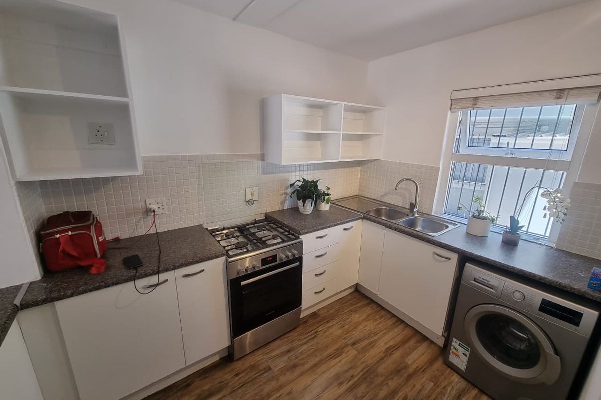 A functional kitchen featuring white cabinetry, a gas stove with oven, double sink, tiled backsplash, and durable laminate flooring.