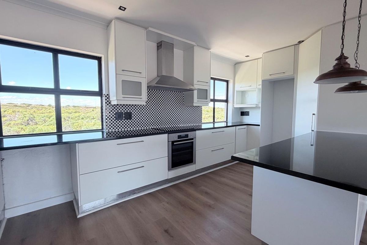 Modern kitchen featuring sleek white cabinetry, black stone countertops, a built-in oven, stainless steel extractor fan, and a striking checkered tile backsplash.