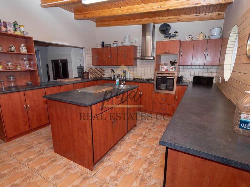 Spacious kitchen featuring wooden cabinetry, dark countertops, built-in oven, extractor fan, and exposed timber ceiling beams with tiled flooring throughout.