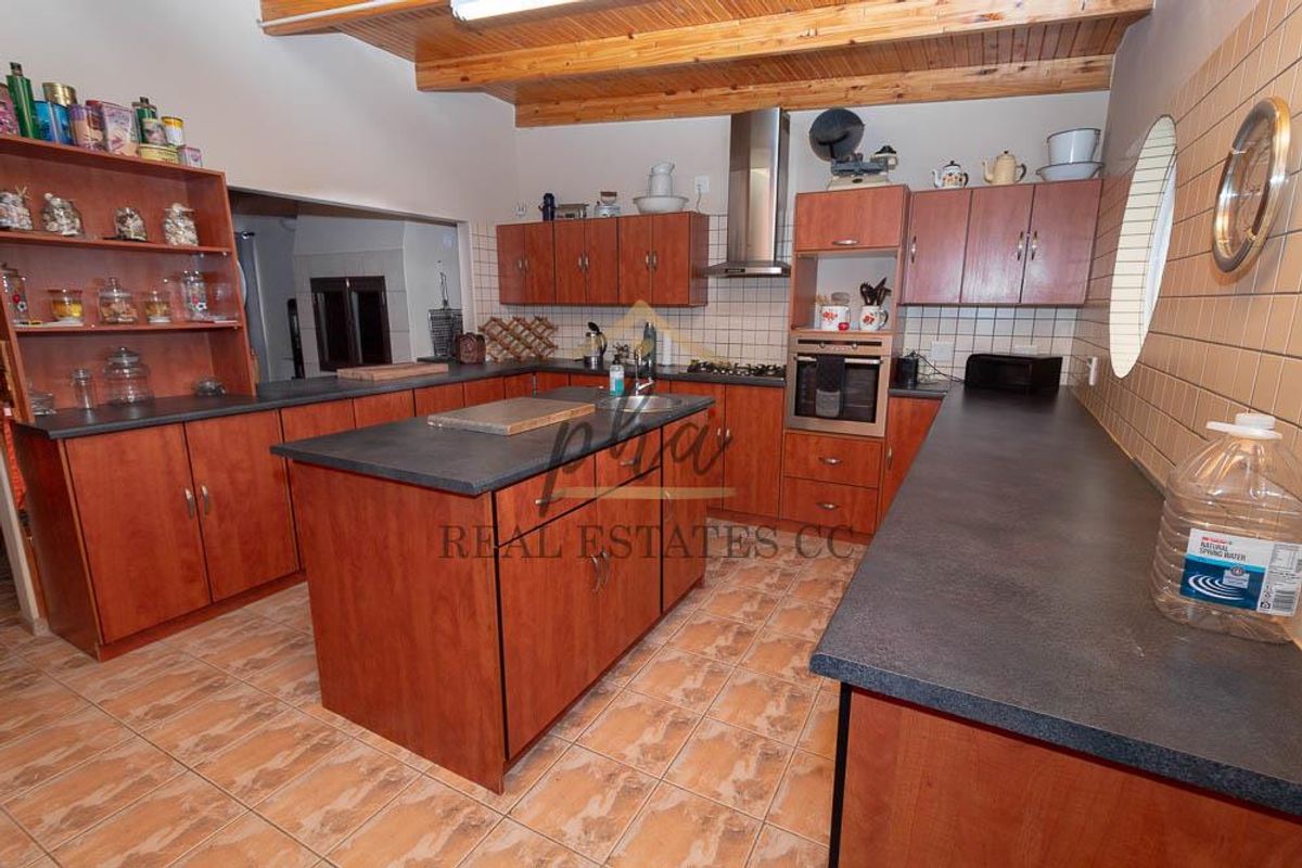 Spacious kitchen featuring wooden cabinetry, dark countertops, built-in oven, extractor fan, and exposed timber ceiling beams with tiled flooring throughout.