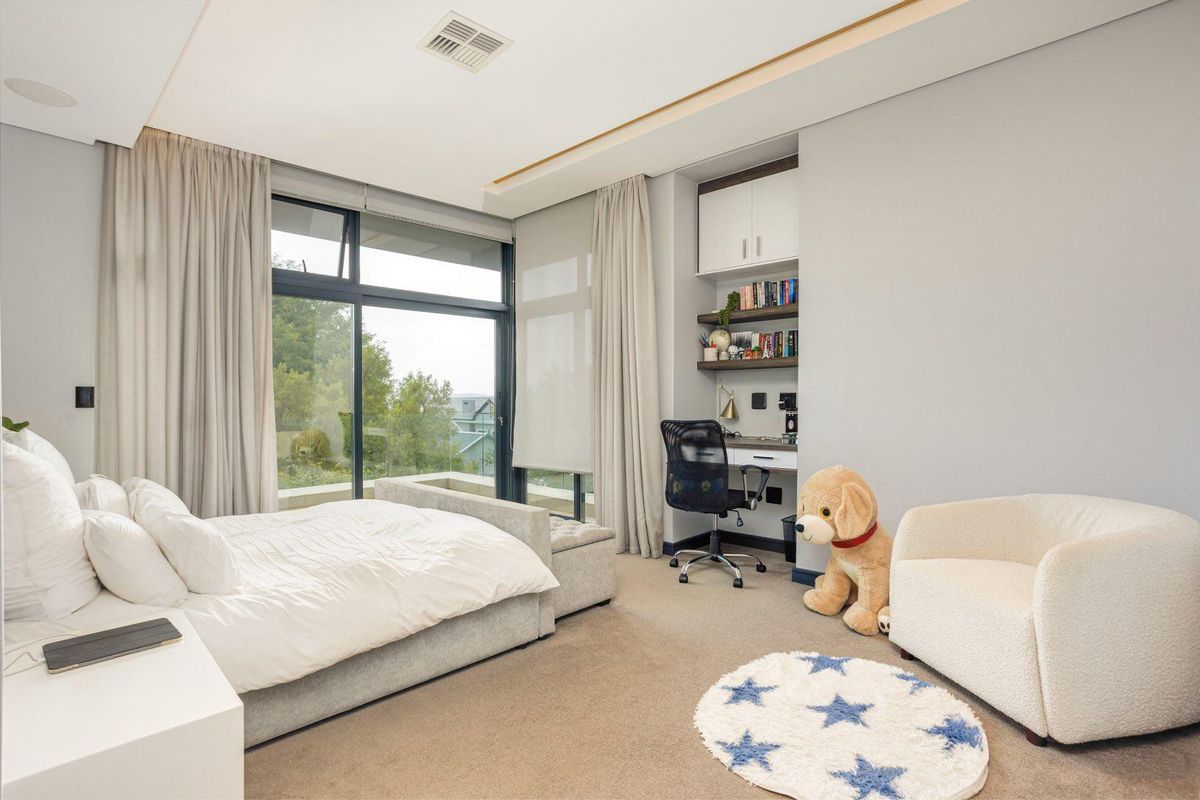 A modern bedroom featuring large sliding glass doors, built-in study nook with shelving, recessed ceiling lighting, and neutral carpeting.