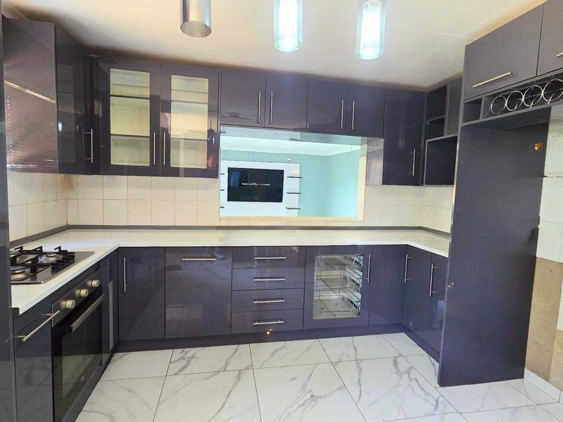 Modern kitchen featuring dark high-gloss cabinetry, built-in oven and gas hob, marble-look floor tiles, and a pass-through window to the living area.