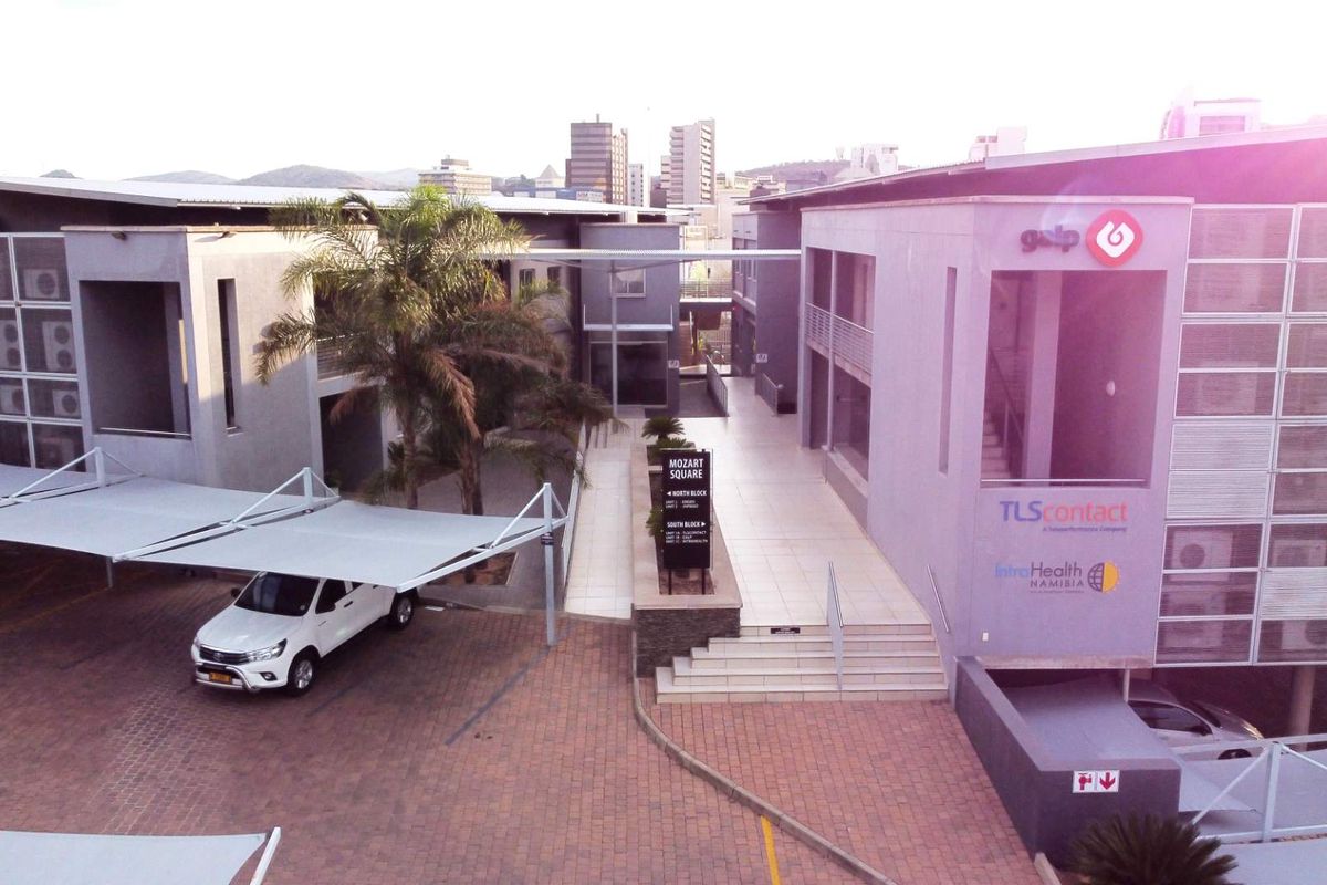 Aerial view of a modern office complex featuring paved parking areas, shade cloth carports, and a central pedestrian walkway between building blocks.