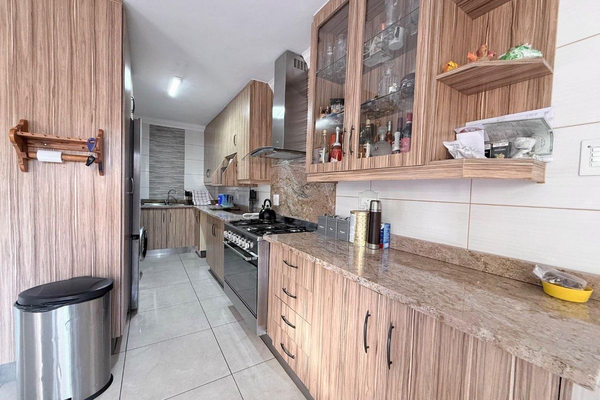 A functional kitchen featuring wood-grain cabinetry, granite countertops, a stainless steel gas stove with extractor fan, and tiled flooring.