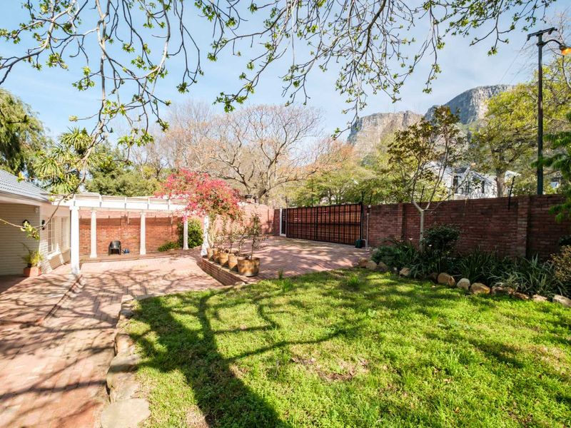 Spacious rear garden featuring brick paving, a pergola, a lawn area, and a secure brick boundary wall with mountain views.
