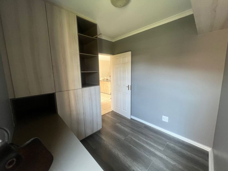 A clean, empty bedroom featuring modern wood-look laminate flooring and built-in storage cabinetry with open shelving.