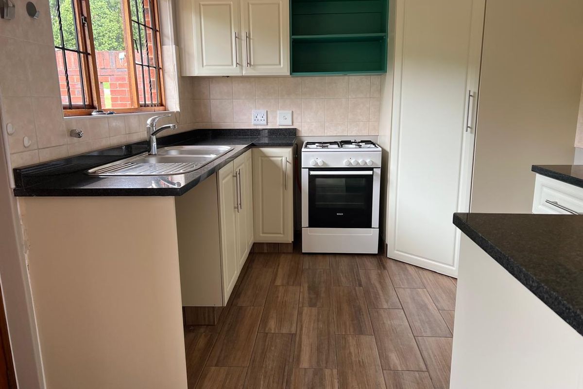 A functional kitchen featuring built-in cabinetry, granite countertops, a stainless steel sink, and a freestanding gas stove with wood-look tiled flooring.
