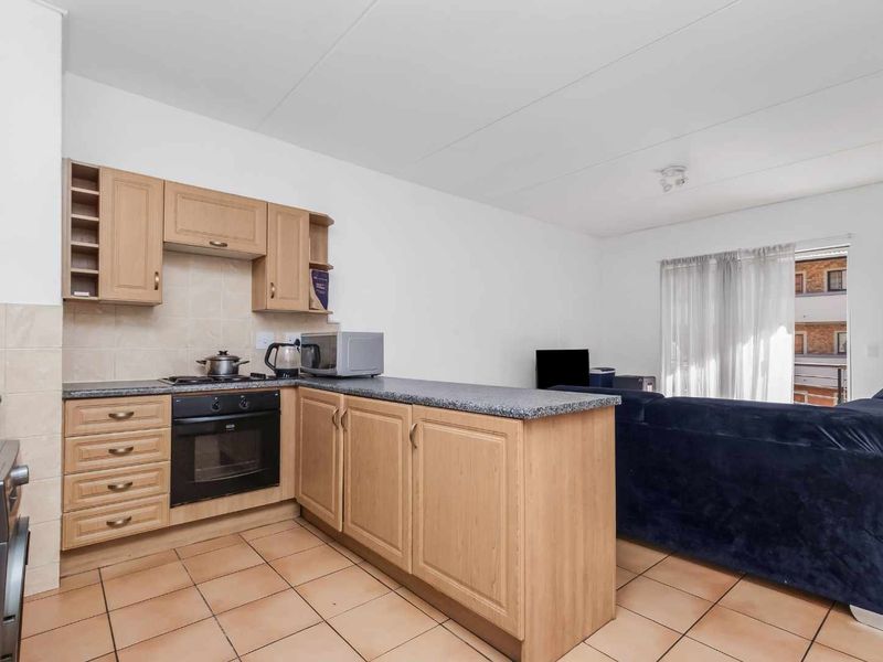 Open-plan kitchen and living area featuring light wood cabinetry, built-in oven, electric hob, and tiled flooring, leading to a balcony.