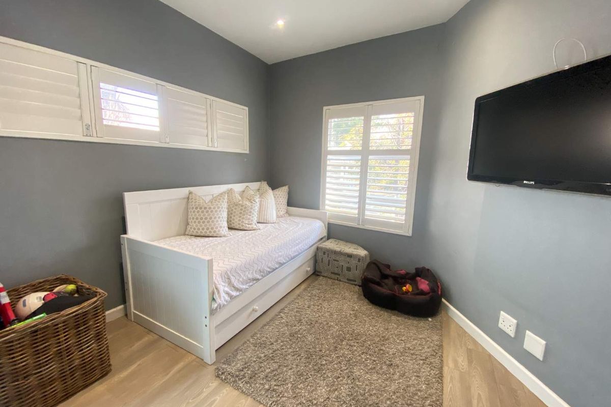 A well-maintained bedroom featuring grey walls, light wood-look flooring, and white plantation shutters on the windows.