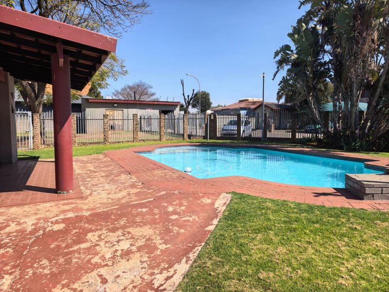 Outdoor pool area featuring a swimming pool, brick paved surround, and a covered patio area with a lawn.