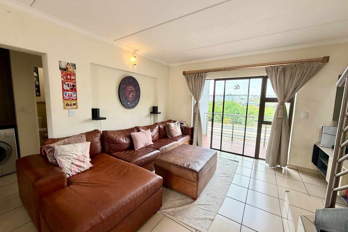 A bright living room featuring tiled flooring and a large sliding glass door that provides access to an outdoor balcony area.