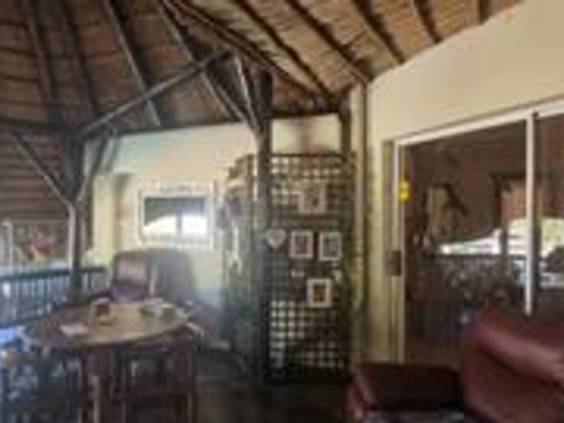 Covered outdoor patio area featuring a traditional thatch roof, exposed timber beams, and sliding glass doors providing access to the main dwelling.