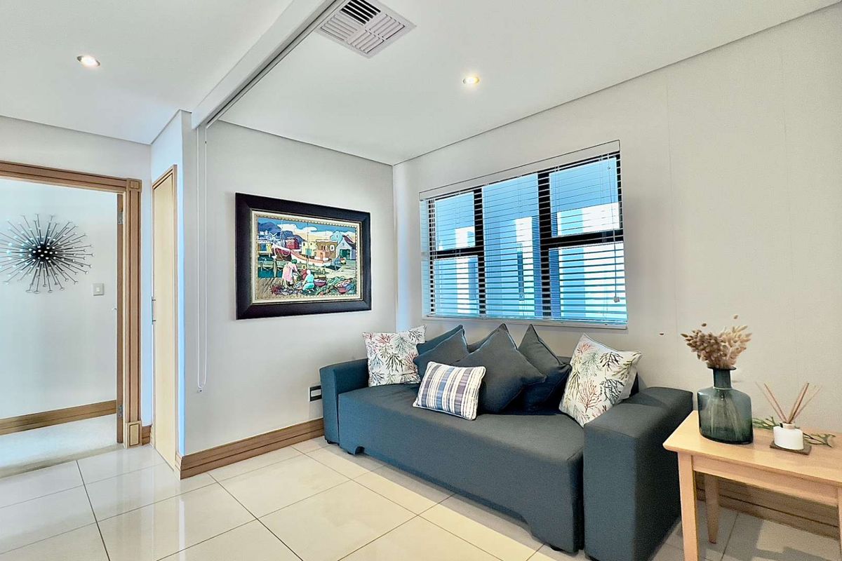 A bright living room featuring neutral tiled flooring, recessed ceiling lighting, and a large window with fitted blinds.