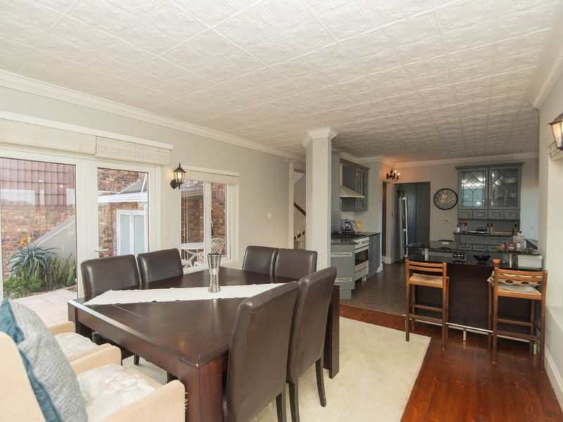 Open plan dining and kitchen area featuring timber flooring, a decorative pressed ceiling, and direct access to an outdoor patio through glass doors.