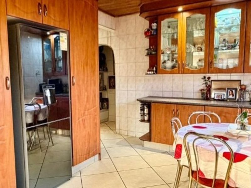 A traditional kitchen featuring warm-toned wooden cabinetry, glass display units, tiled flooring, and a tiled splashback, offering a classic and functional cooking space.