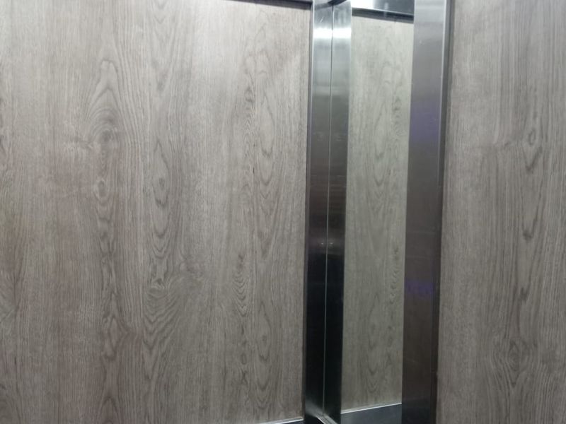 Interior view of an elevator cabin featuring modern wood-look laminate wall paneling and stainless steel trim detailing.