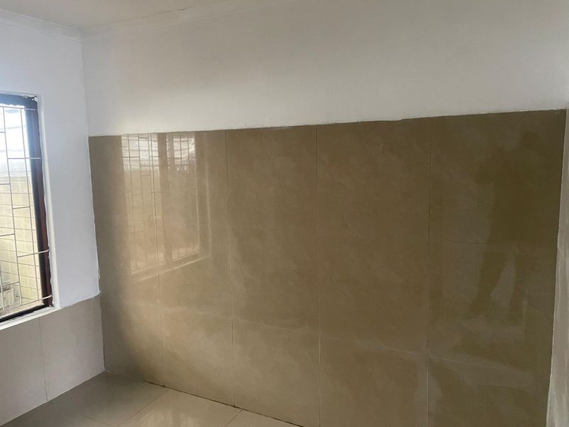 An empty kitchen area featuring large format brown wall tiles and matching floor tiles, with a window fitted with security bars.