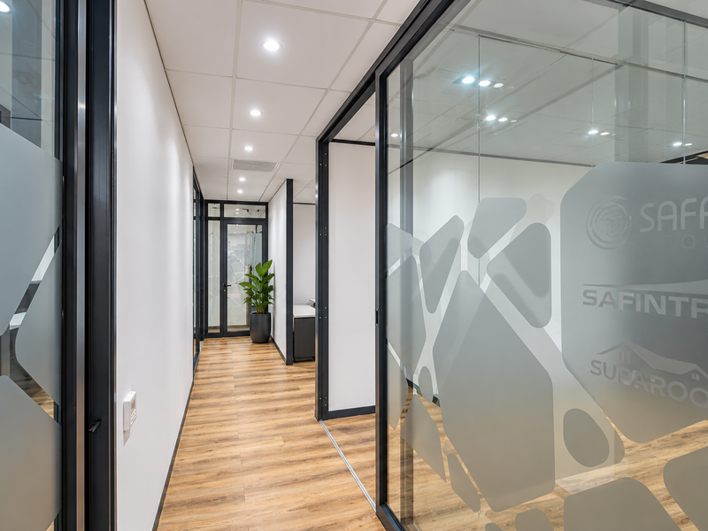 Modern office hallway featuring glass partition walls, wood-look flooring, and recessed lighting, creating a professional and bright workspace environment.