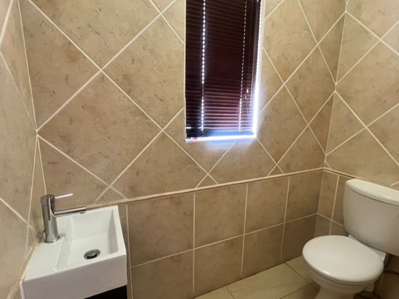 A compact guest bathroom featuring neutral wall tiles, a modern basin, and a standard toilet.