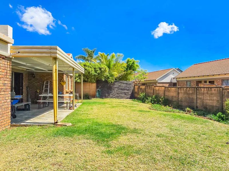 A private rear garden featuring a covered patio area, established lawn, and brick boundary walls, offering a functional outdoor space for the townhouse.