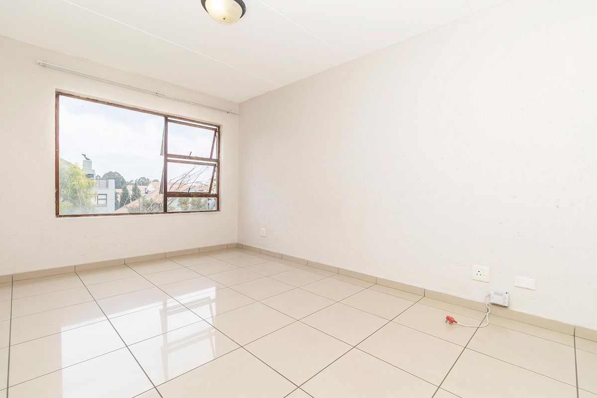 A bright, empty bedroom featuring neutral floor tiles, a large window with exterior views, and a simple ceiling light fixture.