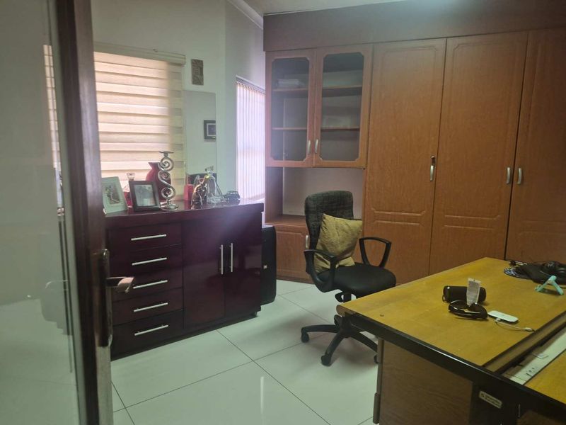 A functional home office featuring built-in wooden cabinetry, tiled flooring, and natural light through roller blinds.