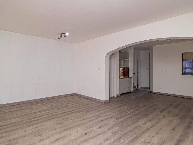 Spacious, light-filled living area featuring modern laminate flooring, a distinctive architectural archway, and neutral finishes, providing a versatile blank canvas for interior design.