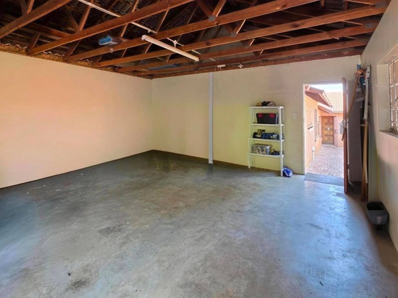 Spacious garage featuring exposed timber roof trusses, a concrete floor, and direct access to the exterior through a side door.