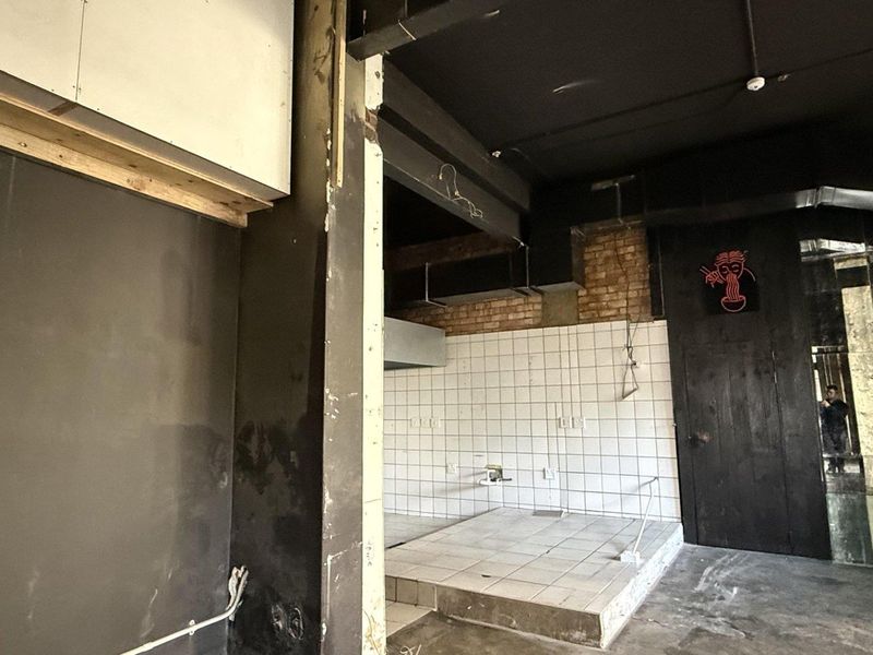 An unfinished commercial kitchen space featuring a raised tiled platform, exposed brickwork, and industrial-style ceiling beams, ready for custom fit-out.