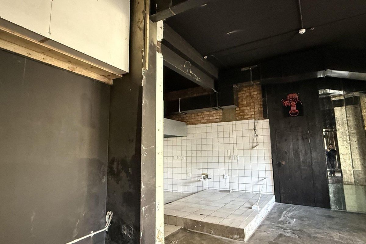 An unfinished commercial kitchen space featuring a raised tiled platform, exposed brickwork, and industrial-style ceiling beams, ready for custom fit-out.