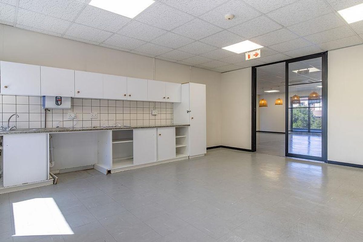 Office kitchenette area featuring built-in cabinetry, tiled backsplash, and sink, with direct access to an adjacent office space through a glass door.