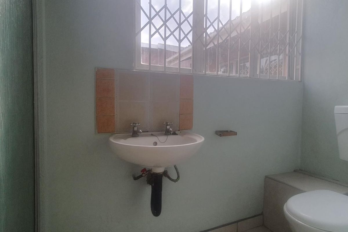 A functional bathroom featuring a wall-mounted basin, toilet, and shower enclosure, equipped with security bars on the window.