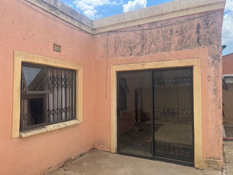 Rear exterior view of the property featuring a sliding glass door, security gates, and a concrete patio area requiring maintenance and repainting.