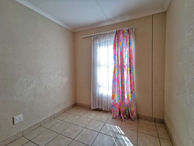 An empty bedroom featuring tiled flooring and a window with a curtain rail, requiring cosmetic updates to the wall finishes.