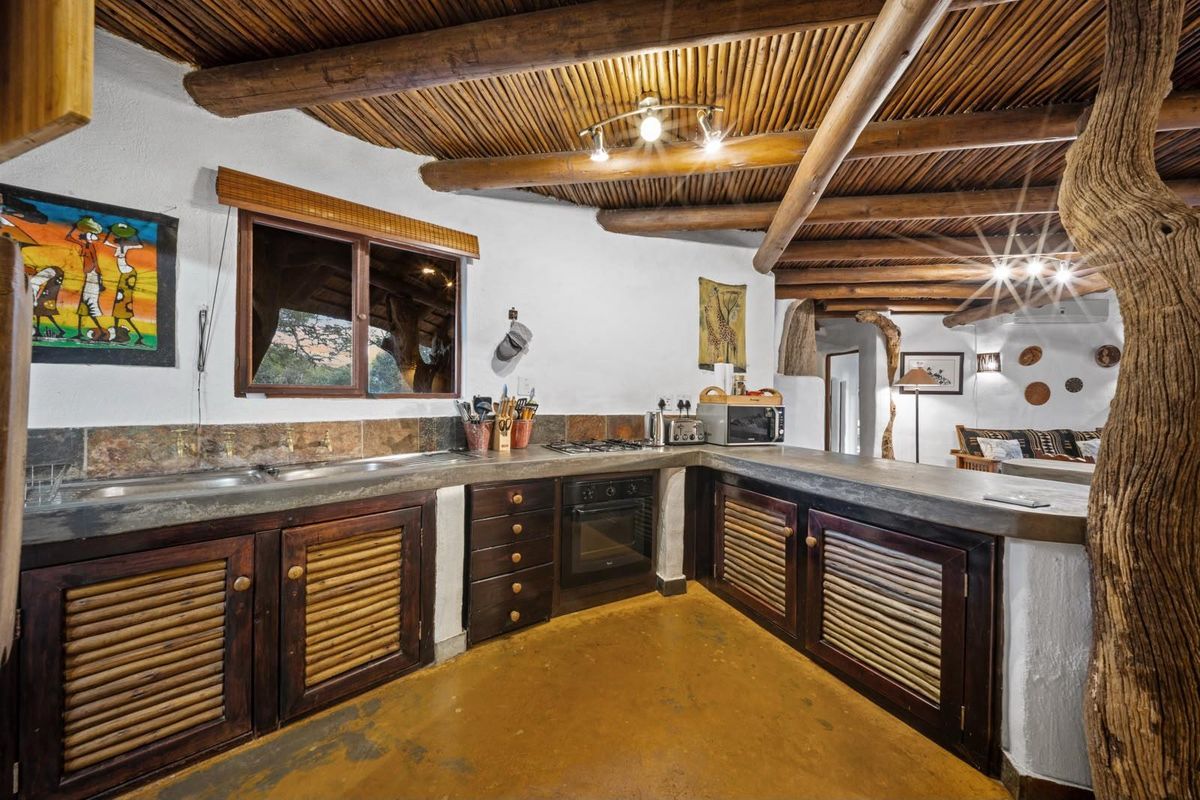 Rustic kitchen featuring concrete countertops, wooden cabinetry with louvered doors, and a unique exposed timber and reed ceiling design.