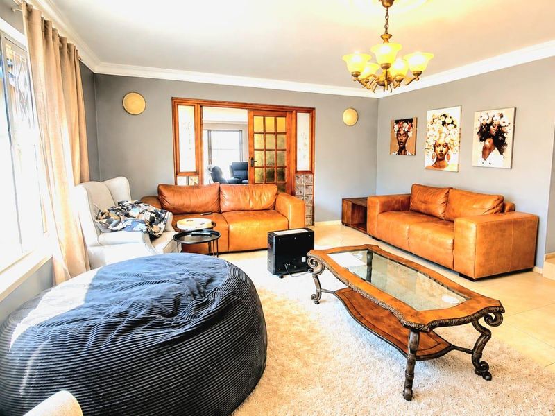 A spacious living room featuring tiled flooring, decorative coving, a classic chandelier, and wooden french doors leading to an adjacent room.