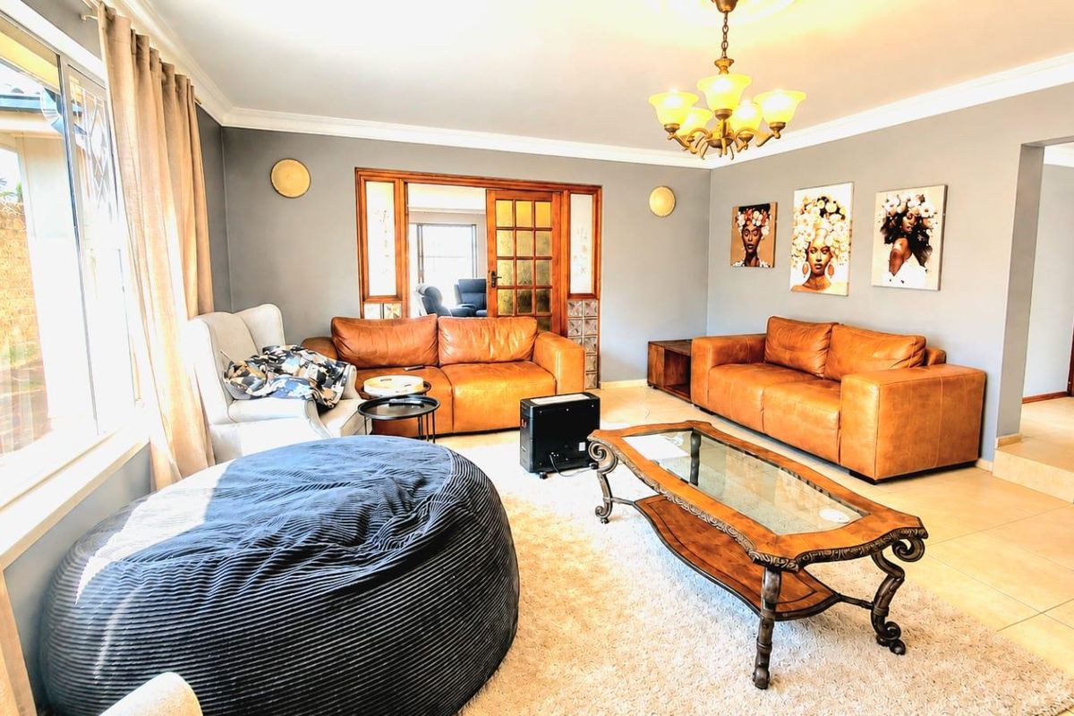 A spacious living room featuring tiled flooring, decorative coving, a classic chandelier, and wooden french doors leading to an adjacent room.