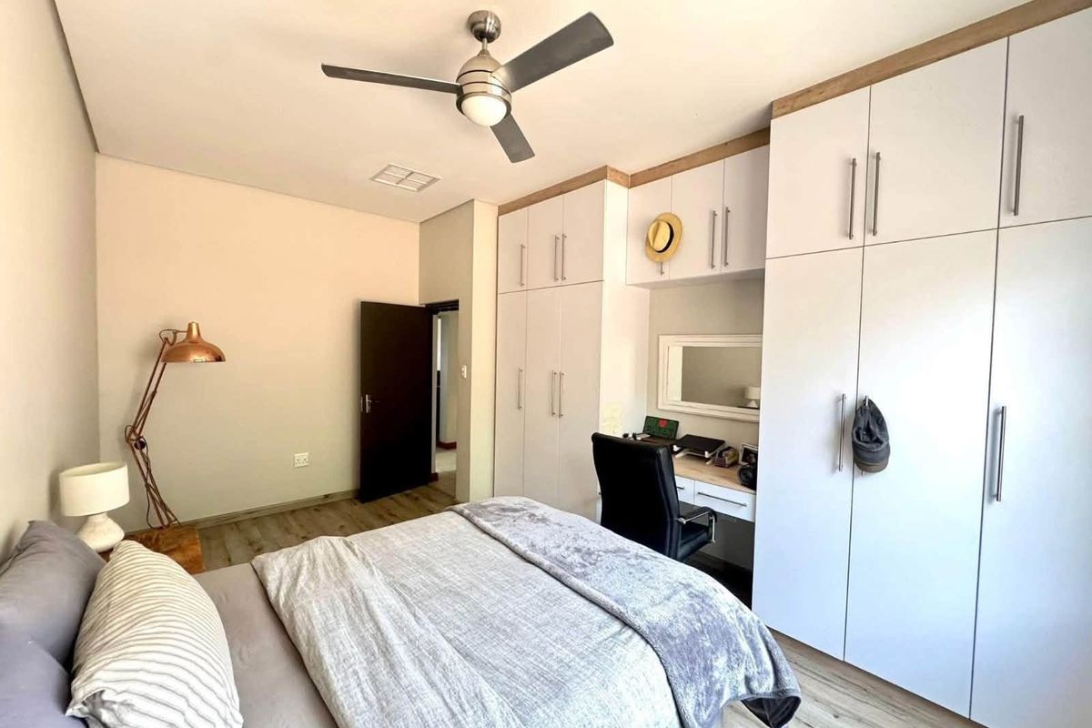 A well-maintained bedroom featuring modern built-in cupboards with an integrated desk, laminate flooring, and a ceiling fan.