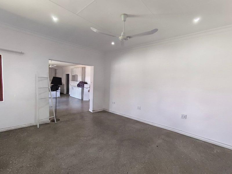Spacious open-plan living area featuring polished concrete floors, recessed lighting, and a ceiling fan, with a clear view into the adjacent kitchen space.