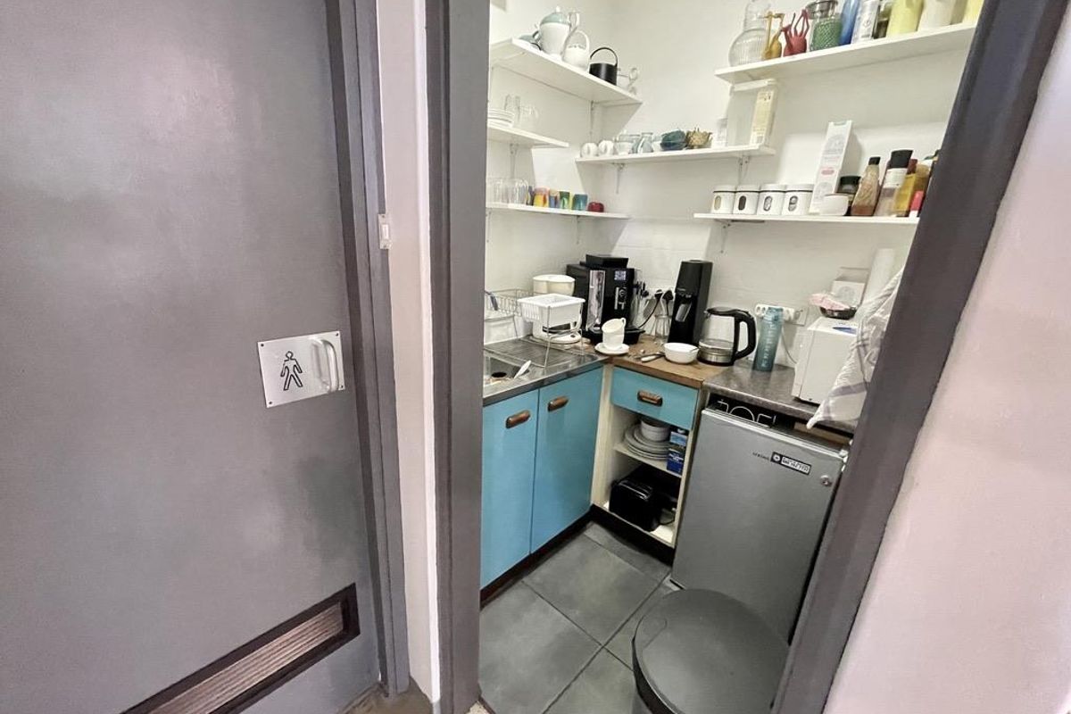 A compact office kitchenette featuring blue cabinetry, a stainless steel sink, open shelving, and tiled flooring.
