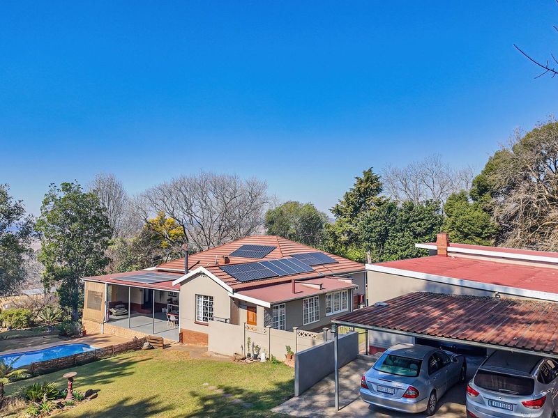 Aerial view of a residential property featuring a tiled roof with solar panels, a swimming pool, a covered patio, and a multi-vehicle carport.