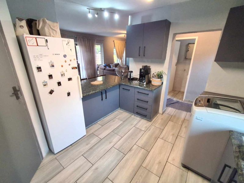 Open plan kitchen featuring modern grey cabinetry, granite countertops, and light wood-look tiled flooring, seamlessly flowing into the adjacent living area.