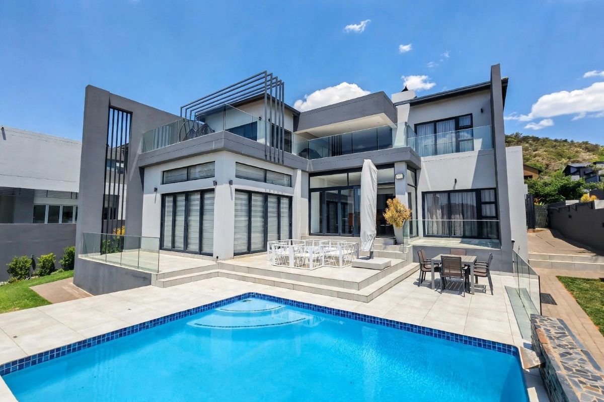 Modern double-story residence featuring a rear patio, glass balustrades, and a swimming pool, showcasing contemporary architectural design and well-maintained outdoor living spaces.